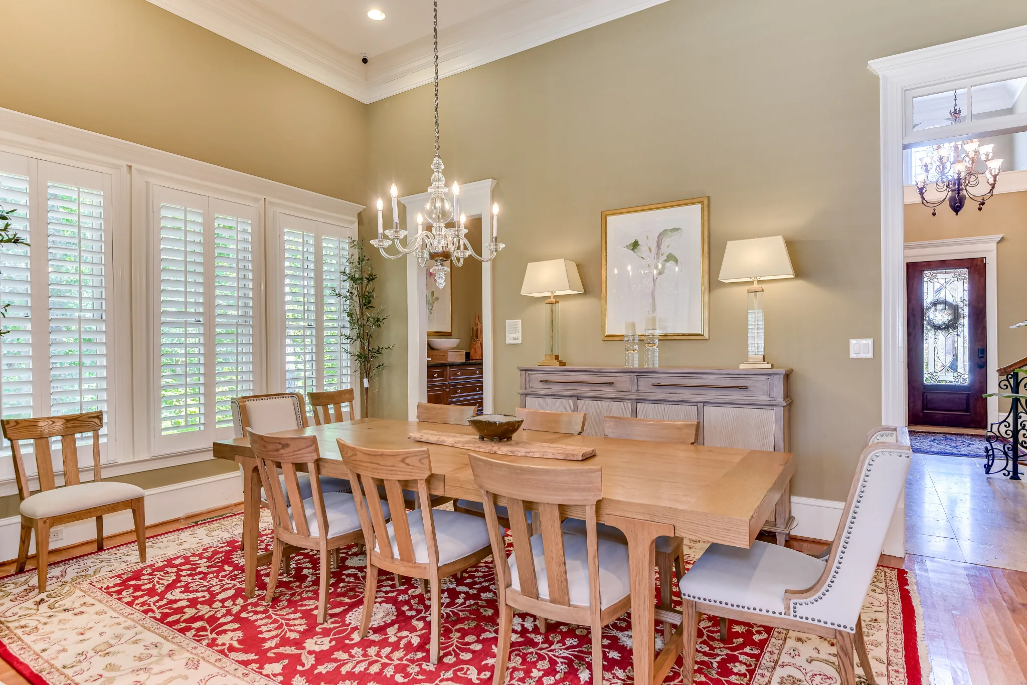 Dining table beneath a chandelier beside tall windows