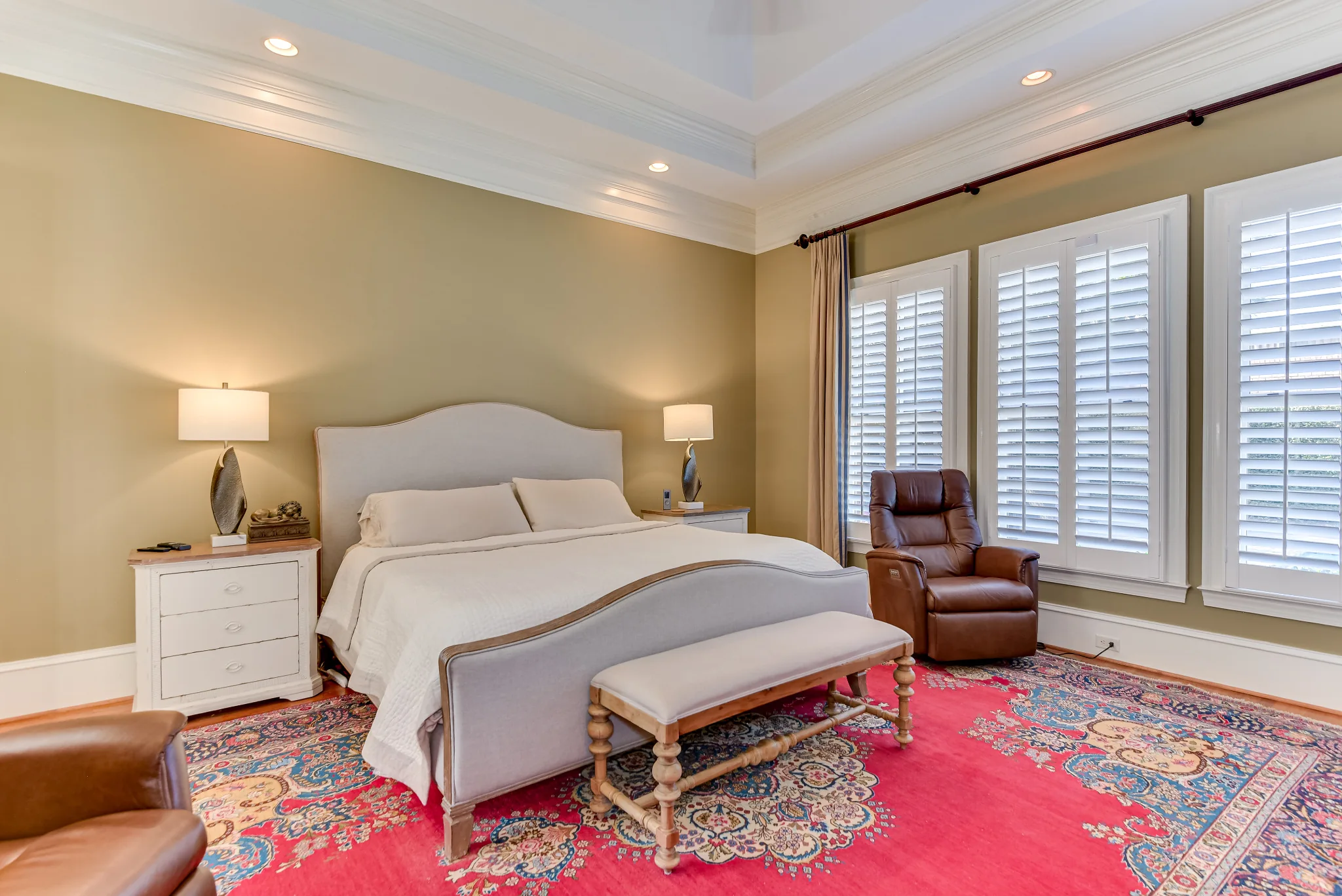 Main-level primary bedroom with a tray ceiling, upholstered bed, and tall windows
