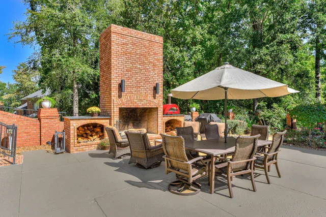 Brick outdoor fireplace beside a dining table and shaded seating